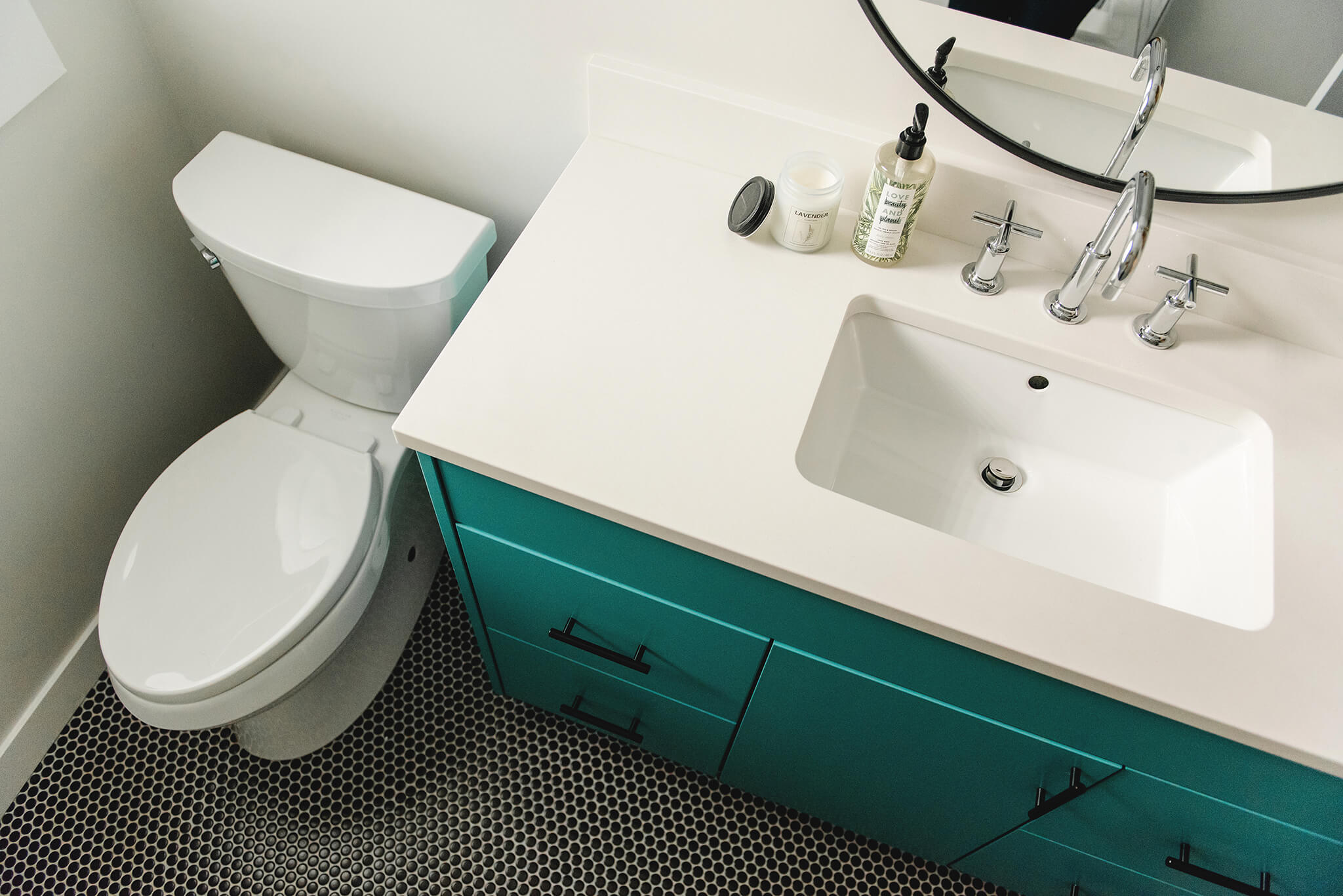 Teal mid-century modern bathroom vanity with black penny tile floor and white countertop