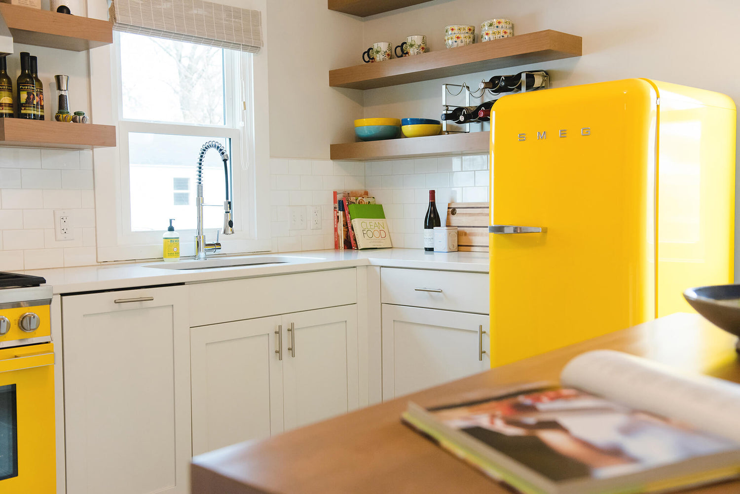 Mid-century modern kitchen with custom white shaker cabinets, yellow SMEG appliances, and floating shelves