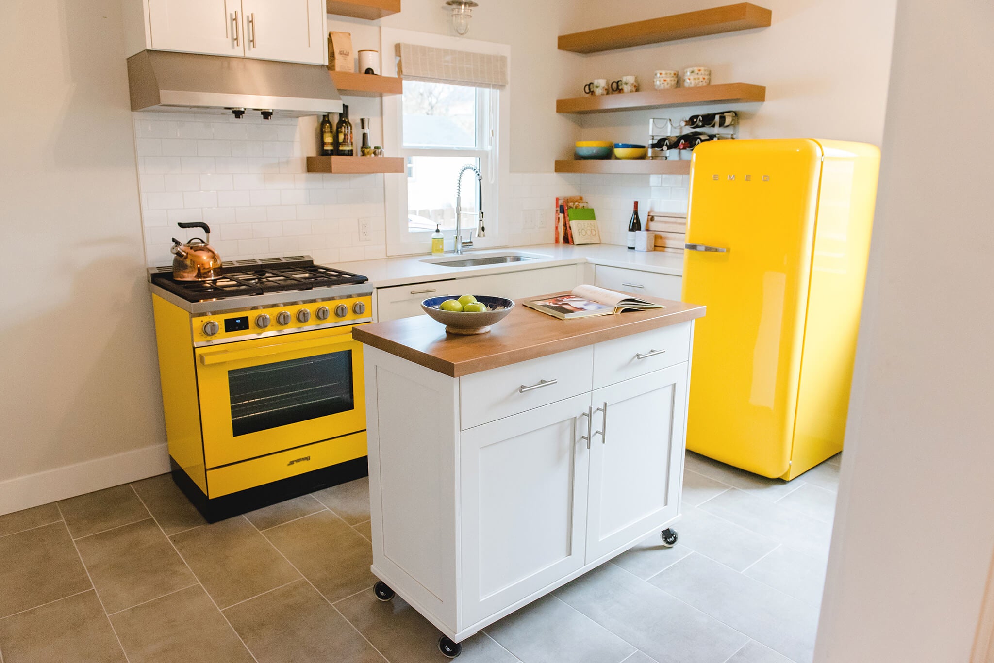 Mid-century modern kitchen with custom white shaker cabinets, rolling kitchen cart, yellow SMEG appliances, and floating shelves