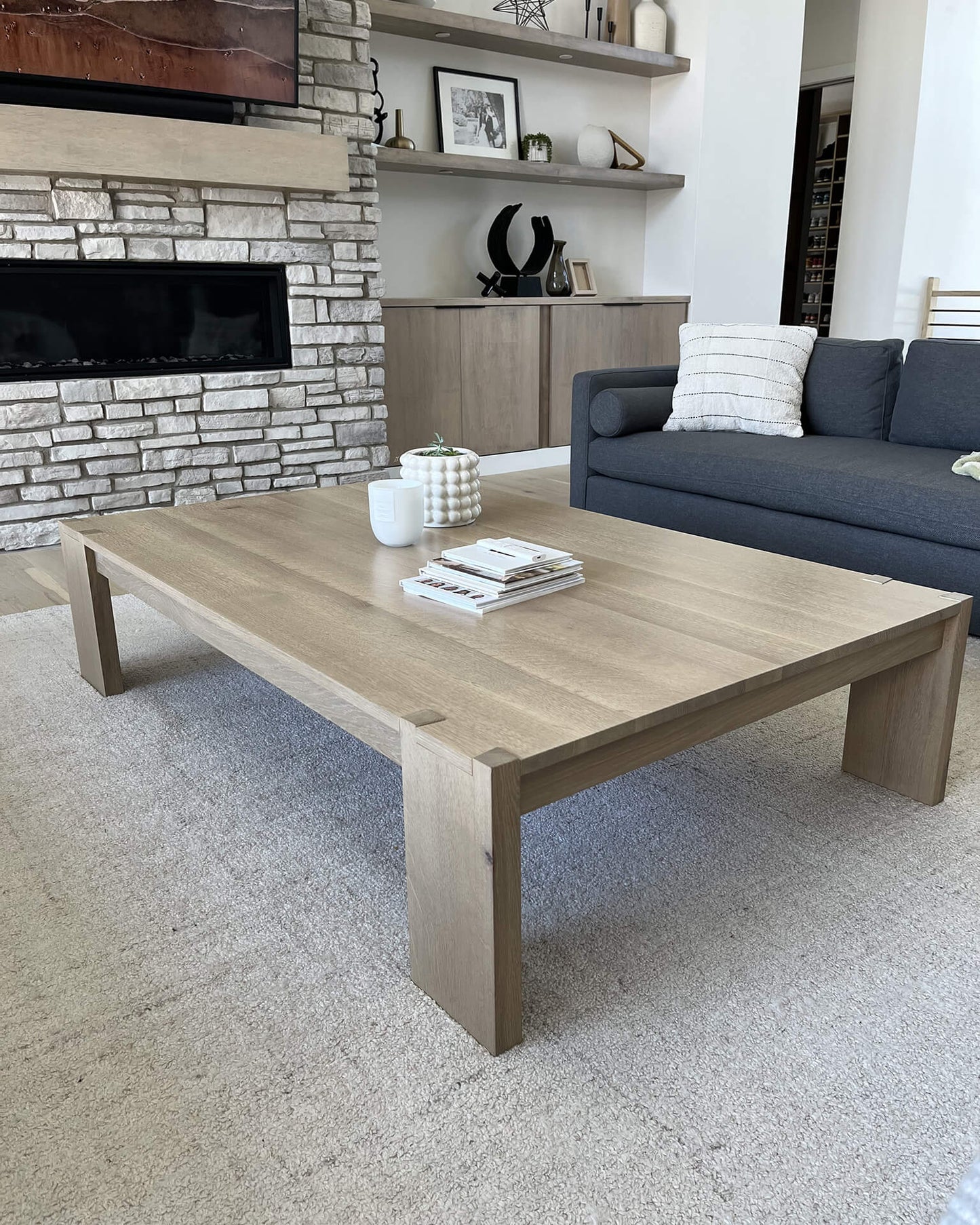 Modern living room with a wooden coffee table, gray sofa, and stone wall.