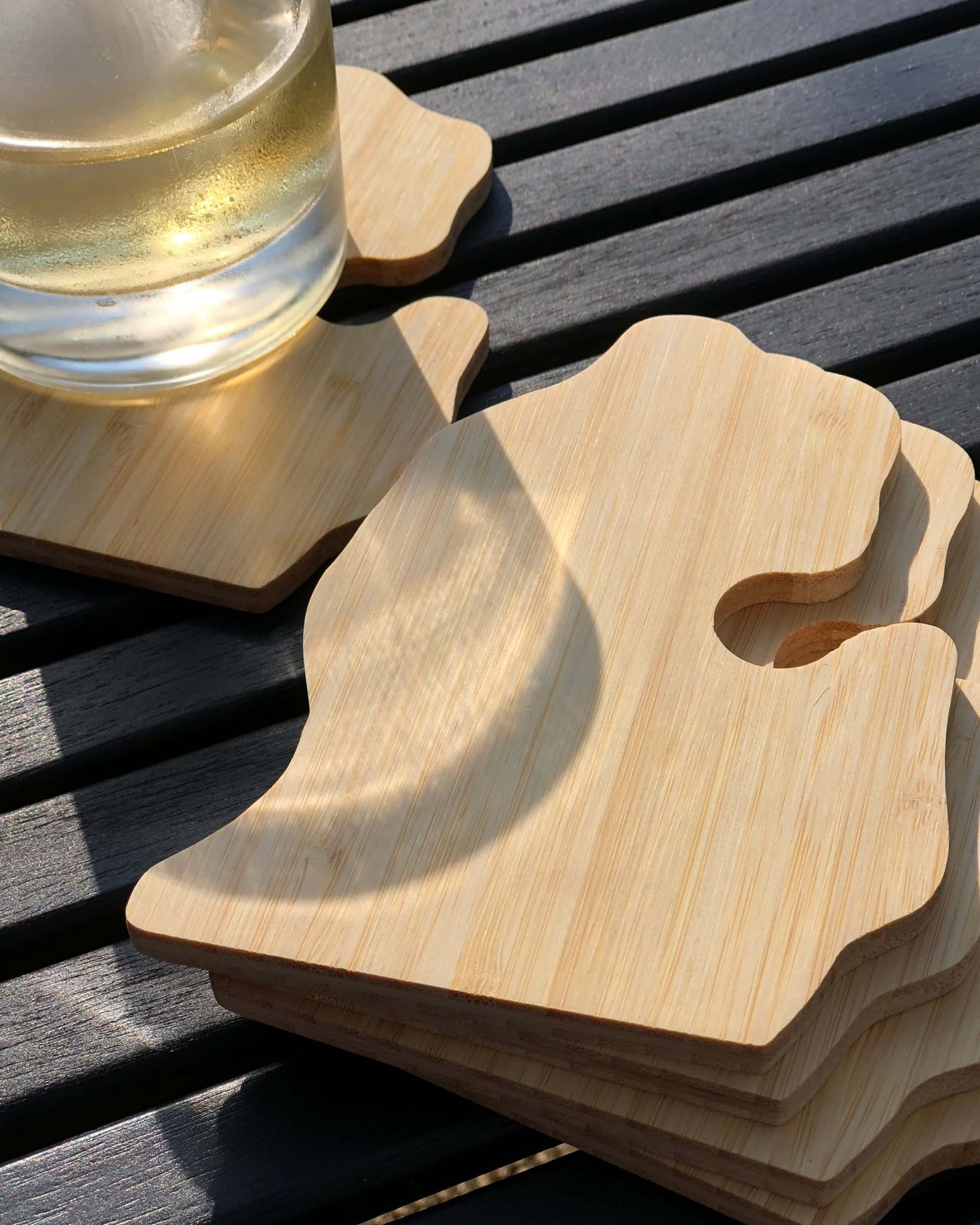 A set of five bamboo coasters shaped like the state of Michigan, with one coaster under a glass of beverage, on a table.